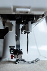 a side view of a sewing machine presser foot on fabric with beige thread visible in the needle