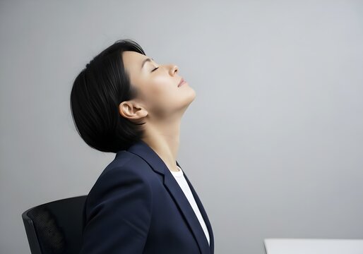 Businesswoman tilting head back looking up for neck stretch and tech neck relief in office profile view
