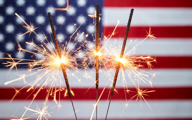 Sparklers ignite and glow brightly against the blurred background of the american flag, celebrating patriotism, independence, and national holidays like the fourth of july