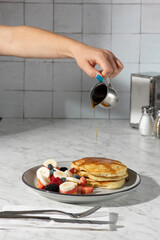 hand pouring syrup on pancakes in hard light