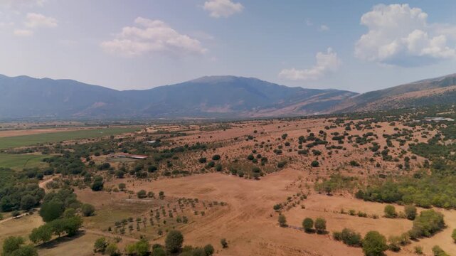 High altitude aerial drone shot gliding over the vast, sunlit summer landscape of the Prosotani region, showcasing green mountains, hills, and fields in Eastern Macedonia, Greece.