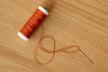 an orange thread spool and a needle with thread lying on a wooden table