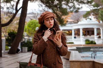 Autumn air surrounds a young stylish woman as she scrolls her smartphone and enjoys a slow walk...