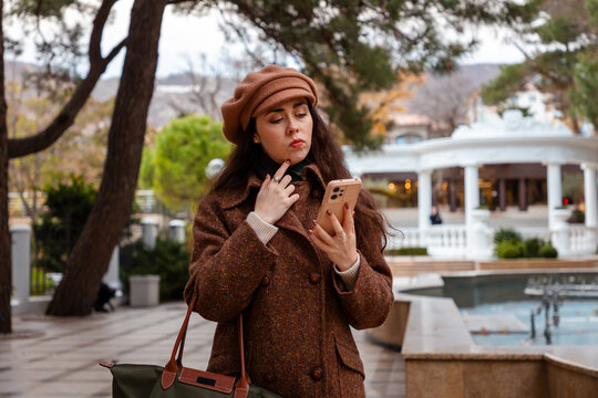 Autumn air surrounds a young stylish woman as she scrolls her smartphone and enjoys a slow walk through the peaceful city streets.