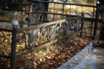 Rusted iron fence with ornate script and fallen leaves at a cemetery grave