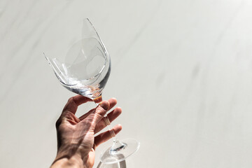 Broken glass of wine in hand on minimalistic white background with shadows