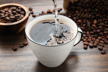 Pouring aromatic coffee into cup and beans at wooden table, closeup