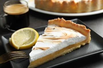 Slice of tasty lemon meringue tart served on black table, closeup