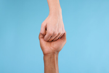 African American man joining hands with his partner on light blue background, closeup