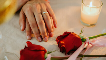 Couple's hands with engagement ring showing intimacy and romance, celebrating love with a glowing candle and beautiful red roses on a romantic dinner setup