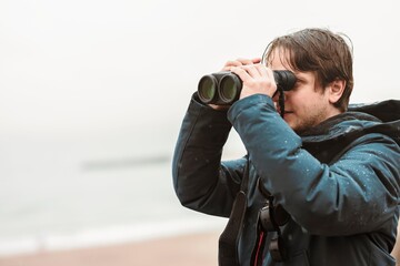 Obraz premium A person stands on the sandy beach, focusing on the horizon with binoculars. Fog blankets the Black Sea, creating a serene atmosphere as waves gently flow
