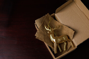 Golden deer figurine in an eco craft gift box on dark background with soft contrast and clear copy space. Concept of authentic handmade packaging, individual holiday decoration and marketing visuals.