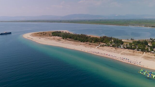 High aerial drone circling shot over the Thracian Sea and the pristine white sands of Keramoti Blue Flag Beach, Kavala, Greece, featuring lush coastal pine forests.