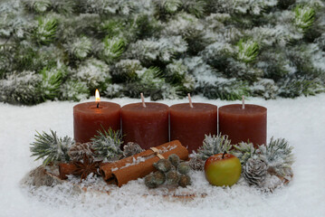 Erster Advent: Eine Dekoration aus braunen Kerzen, Zimtstangen, Anis und Äpfeln vor einer Kulisse...