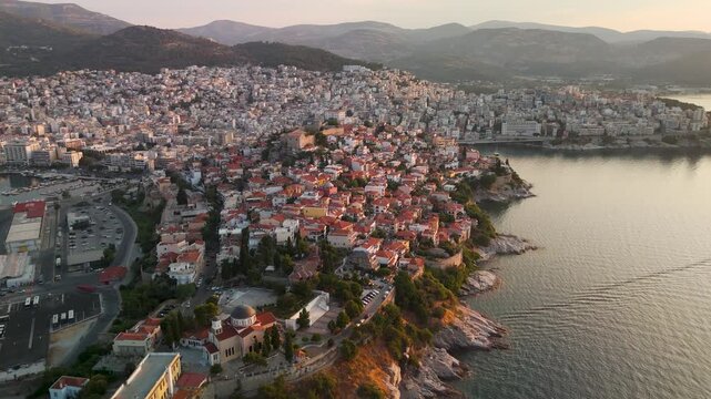 Golden hour aerial drone pan out from the historic Acropolis Fortress and colorful houses of the Panagia Old Town Peninsula, revealing the city of Kavala and the Thracian Sea, Greece.