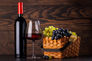 Naklejka premium Red wine bottle with a glass and basket of fresh grapes