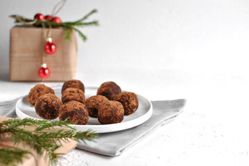 Chocolate truffles coated in cocoa sit on a white plate with soft holiday décor in the background, creating a cozy and festive winter atmosphere.