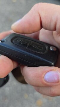 Hand pressing car key button to unlock vehicle closeup vertical video. female hand and fingers pressing unlock button on car remote fob. opening a vehicle on parking area