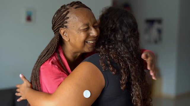 Happy african mother hugging daugher with diabetes patch at home - Family love, lifestyle and disease concept
