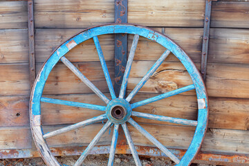 Vintage wooden wagon wheel in front of weathered wooden wall.