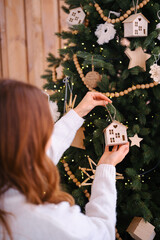 Person decorating Christmas tree with small wooden houses and warm lights