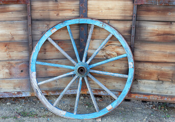 Vintage wooden wagon wheel in front of weathered wooden wall.