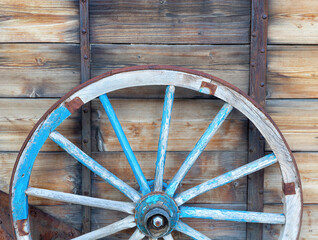 Vintage wooden wagon wheel in front of weathered wooden wall.