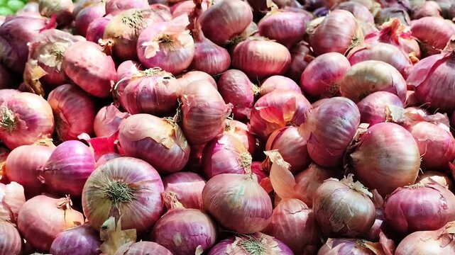 A close-up view of fresh red onions stacked in bulk at a local market. Great for agriculture, organic produce, kitchen ingredients, food backgrounds and vegetarian cooking themes.