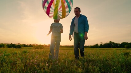 Family team, sports games. Child daughter play football with father on lawn. Girl child, parent running after big ball in park. Active happy family, child dad cheerfully playing ball on green grass