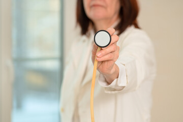 Female healthcare professional holds and applies stethoscope diaphragm during patient exam. Focus on chest sounds, respiratory diagnosis, pneumonia, bronchitis, and health care.