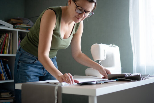 Dressmaker carefully measuring the cloth with a measuring tape on her worktable, ensuring precision for her sewing project. - Powered by Adobe