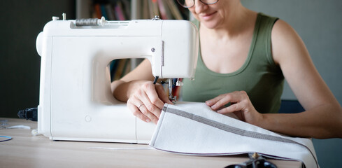 Horizontal banner. Closeup of skilled female hands operating a sewing machine, guiding textile under the fast moving needle.