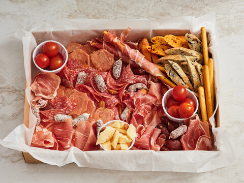 A beautifully arranged charcuterie board showcases a variety of cured meats, cheeses, fresh tomatoes, and crunchy snacks. Perfect for a party or casual gathering