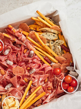 A beautifully arranged charcuterie board features various sliced meats, cheeses, crackers, nuts, and cherry tomatoes. Perfect for sharing at a casual get-together