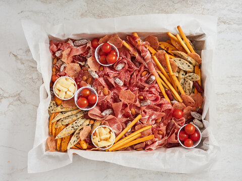 A colorful charcuterie board showcases an array of meats, cheeses, cherry tomatoes, and snack sticks, all neatly arranged on a marble countertop. Perfect for gatherings or celebrations