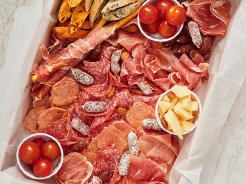 A large serving tray displays an assortment of cured meats like prosciutto and salami, paired with cheeses, nuts, and cherry tomatoes, perfect for a gathering