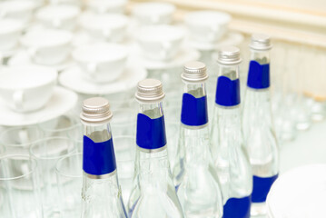 Elegant beverage and dining setup. A sophisticated arrangement featuring glass bottles with blue labels, surrounded by neatly arranged cups and saucers.