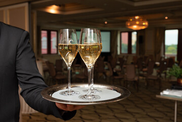 Waiter holds two champagne glasses on a silver tray set the scene for a refined event within a stylish banquet hall. the setting is perfect for weddings, celebrations, or upscale gatherings.
