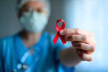 Nurse or doctor in medical uniform holds in hand red satin awareness ribbon, symbolizing HIV AIDS solidarity, support and hope for future treatment.