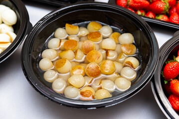 A black bowl filled with golden caramelized baby potatoes in a light syrup, surrounded by fresh strawberries. perfect for enhancing culinary presentations and recipes.
