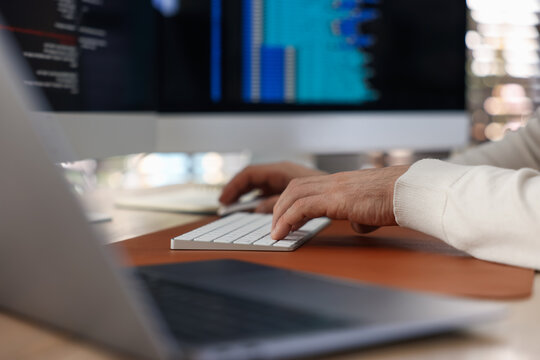 Programmer working on laptop at wooden table indoors, closeup