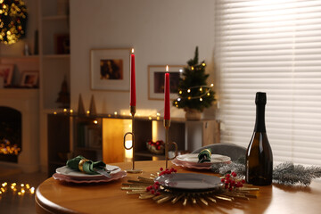 Christmas table setting with plates, wine and burning candles in festive decorated room