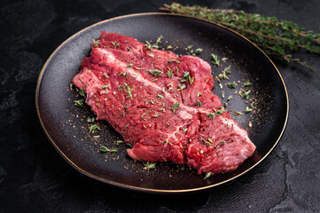Raw hanger tender beef steak, skirt steak on plate with herbs and spices. black background. top view