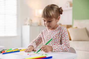 Cute little girl drawing with felt pen at white table indoors