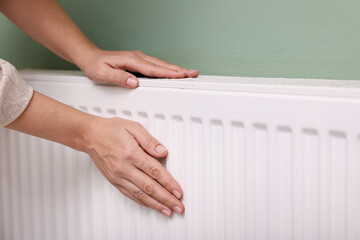Woman warming her hand near radiator indoors, closeup