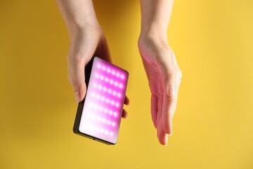 Woman with glowing LED lamp on yellow background, closeup