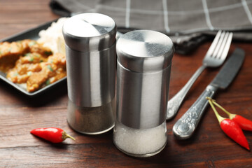 Salt, pepper shakers, chili and chicken tikka masala on wooden table, closeup