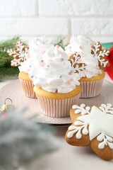 Tasty cupcakes with Christmas decor and gingerbread cookies on white table, closeup