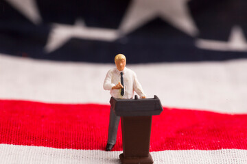 A figurine of a man stands on a podium against the backdrop of the US flag.