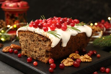 Tasty Christmas cake with icing, cranberries, nuts and festive decor on black table, closeup